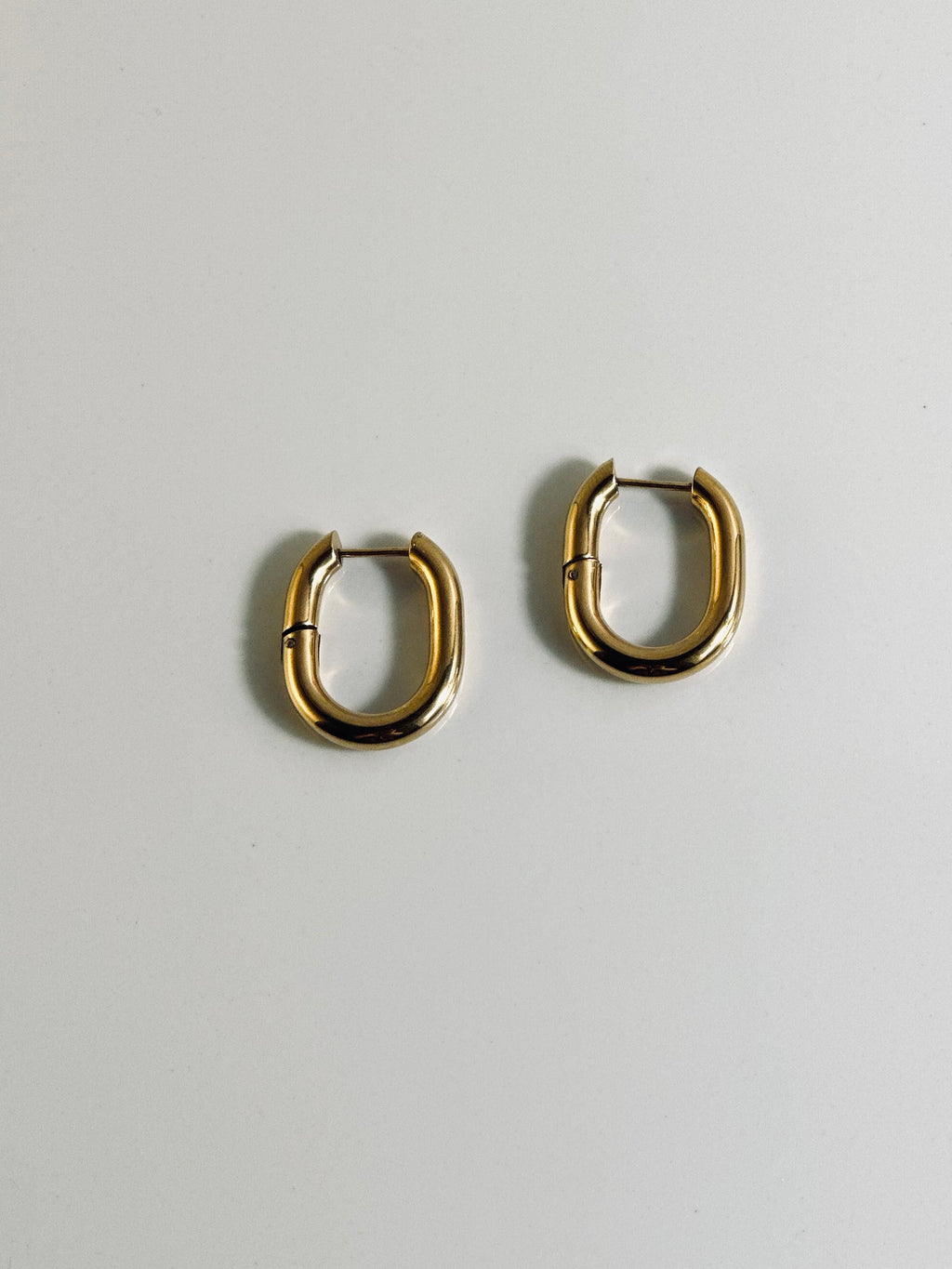 Vera Hoop earrings from the “Timeless Grace” collection displayed flat, showcasing their bold 1-inch 18k gold-plated design. The chunky shape and radiant finish reflect strength and elegance, made to last with hypoallergenic and tarnish-resistant quality.