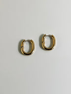 Vera Hoop earrings from the “Timeless Grace” collection displayed flat, showcasing their bold 1-inch 18k gold-plated design. The chunky shape and radiant finish reflect strength and elegance, made to last with hypoallergenic and tarnish-resistant quality.