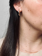 Serena — Gold Box Chain Necklace from the Timeless Grace collection, worn by a model and paired with gold hoop earrings. The thin, gold-plated brass chain rests gently on the collarbone, highlighting effortless layering and everyday elegance, evoking confidence, grace, and polished simplicity.