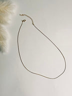 Serena — Gold Box Chain Necklace from the Timeless Grace collection, a thin gold-plated brass chain displayed on a book with focus on the lobster clasp and 2-inch extender. The delicate links and adjustable design highlight both elegance and practicality, symbolizing versatility, grace, and effortless style.