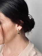 The Vera Hoop earrings worn by a model, their chunky 18k gold-plated design catching the light with a soft glow. The timeless hoops frame the face beautifully, expressing confidence, elegance, and enduring grace.