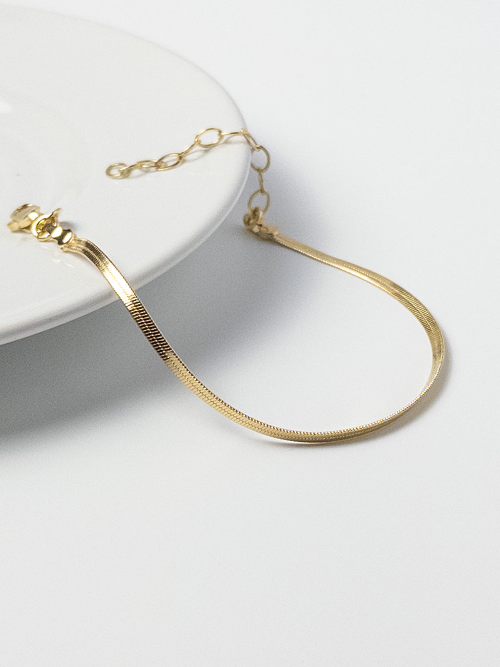 Lumen Bracelet displayed on the edge of a tabletop, highlighting the 18k gold filled snake chain and clasp detail from the Weightless Collection.