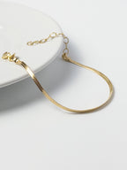 Lumen Bracelet displayed on the edge of a tabletop, highlighting the 18k gold filled snake chain and clasp detail from the Weightless Collection.