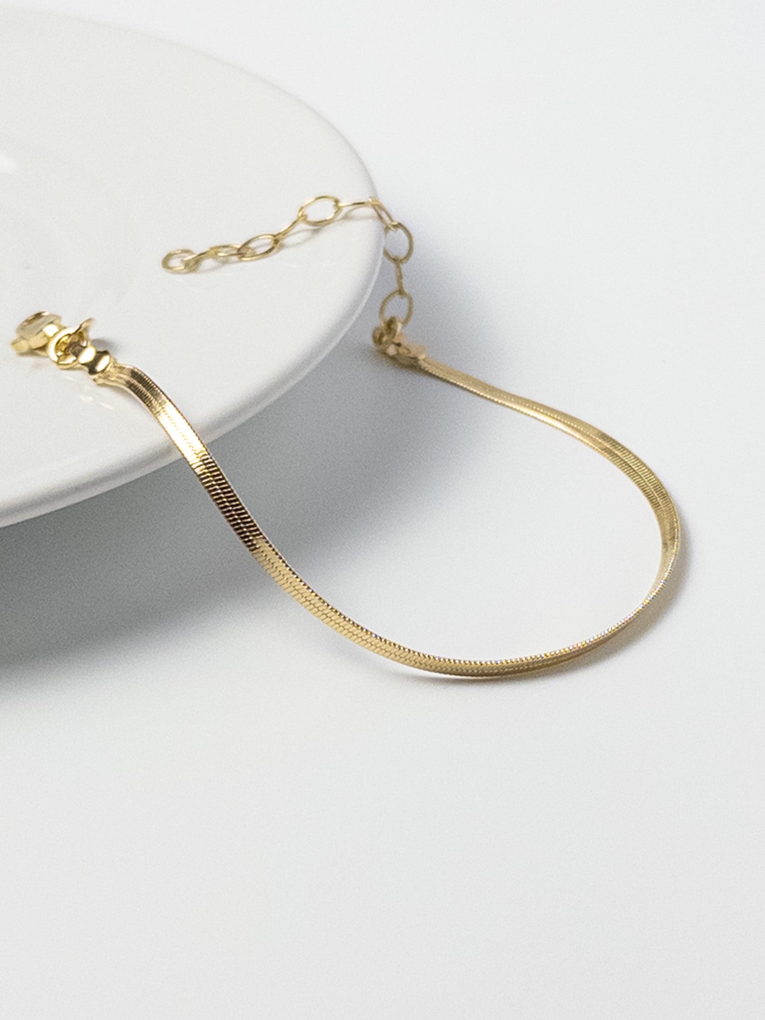 Lumen Bracelet displayed on the edge of a tabletop, highlighting the 18k gold filled snake chain and clasp detail from the Weightless Collection.