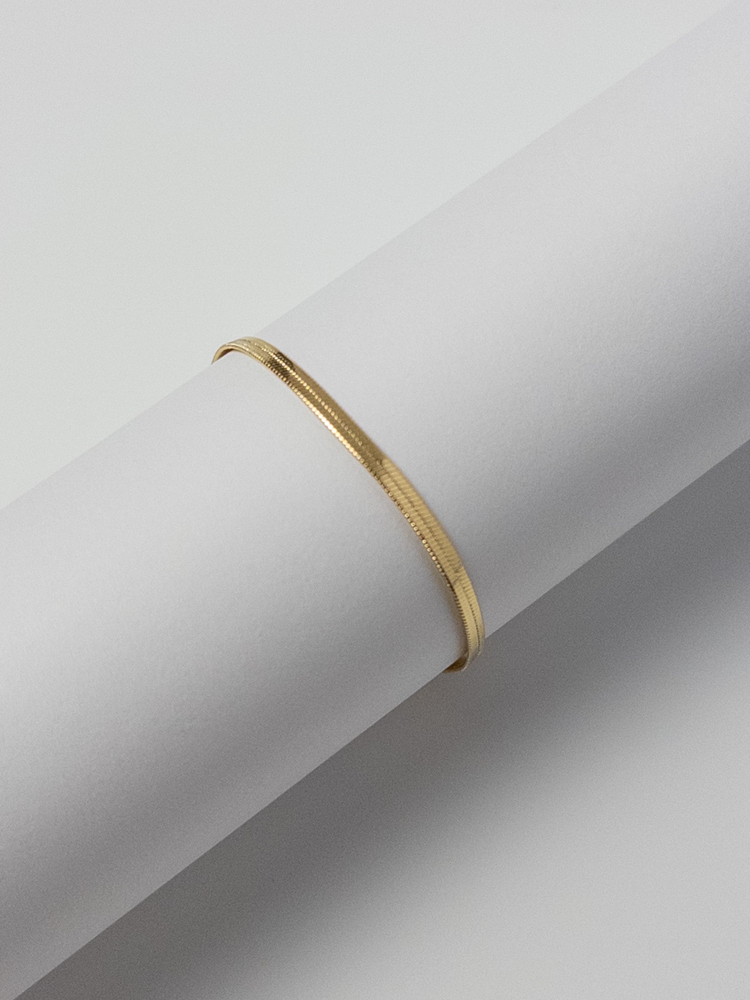 Lumen Bracelet front view displayed on a round bracelet stand, featuring a minimalist 18k gold filled snake chain design from the Weightless Collection.