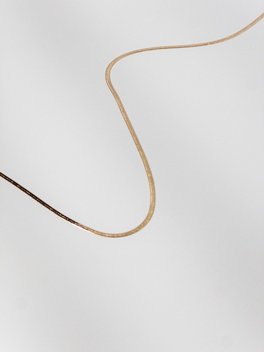 Lumen Chain snake necklace displayed in a wave flat lay to showcase the smooth flexible gold chain detail.