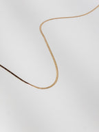 Lumen Chain snake necklace displayed in a wave flat lay to showcase the smooth flexible gold chain detail.
