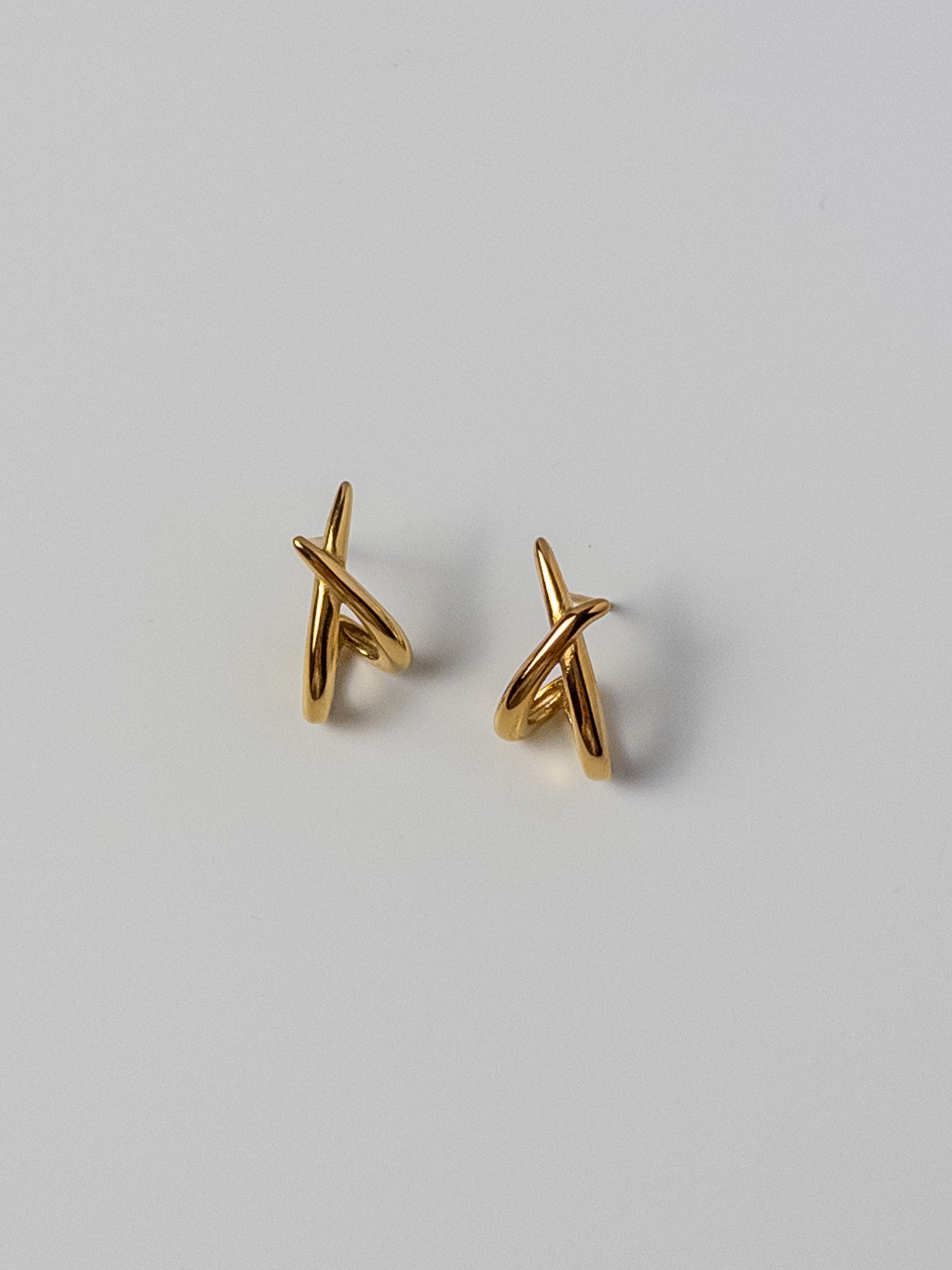 Lumen Studs gold crossover stud earrings featuring a minimalist intertwined design for everyday wear.