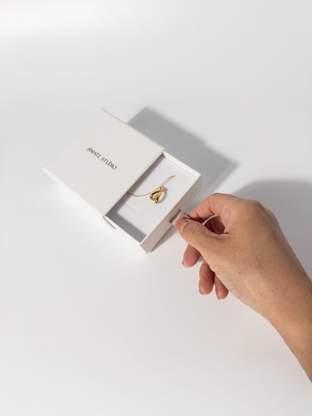 Amate Studio Lumen Studs and Lumen Chain necklace in an elegant drawer-style jewelry box, partially opened with a hand pulling the ribbon to reveal the 18k gold filled jewelry inside.