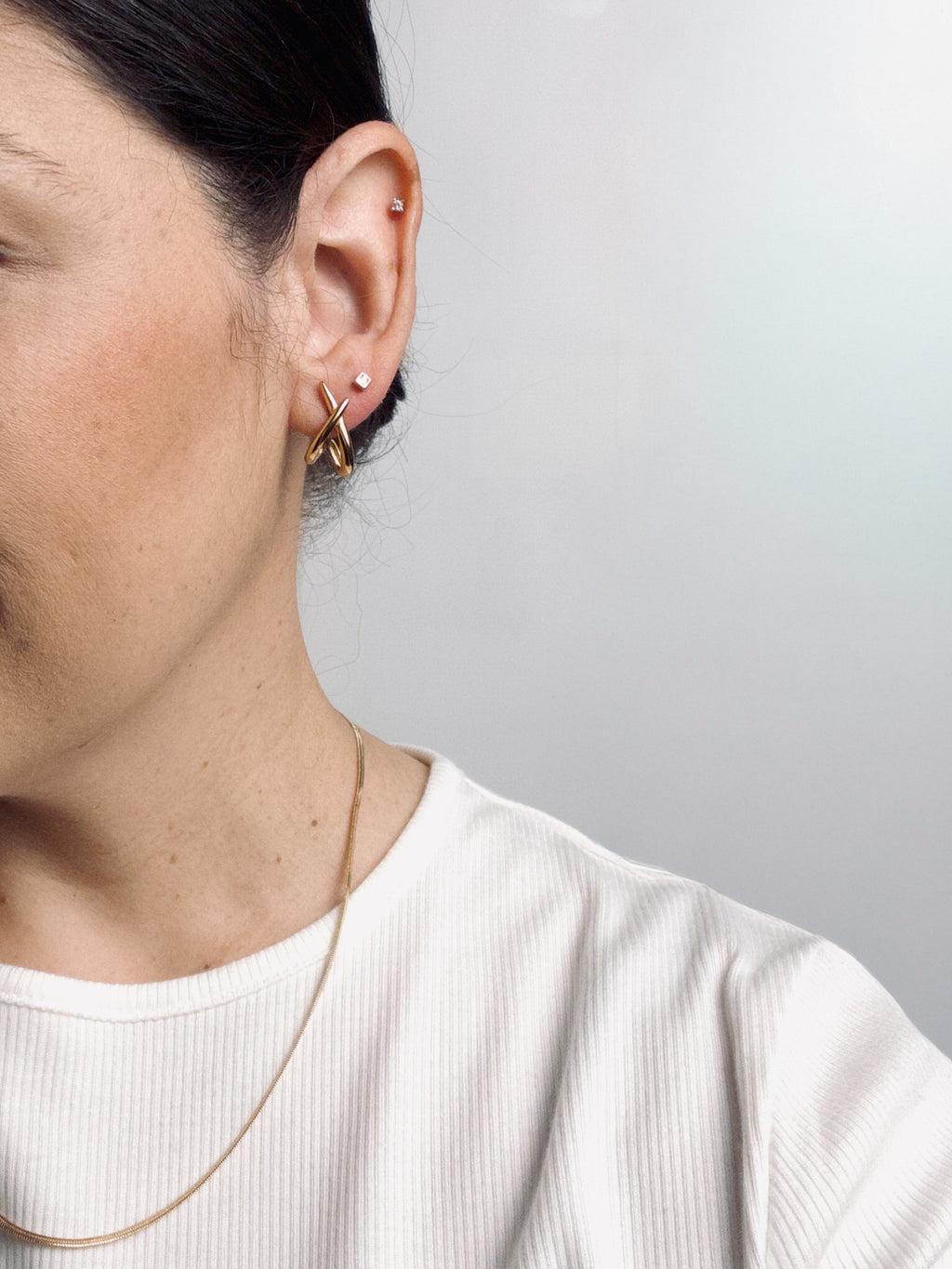 Model wearing Lumen Studs gold crossover earrings paired with a gold snake chain necklace.