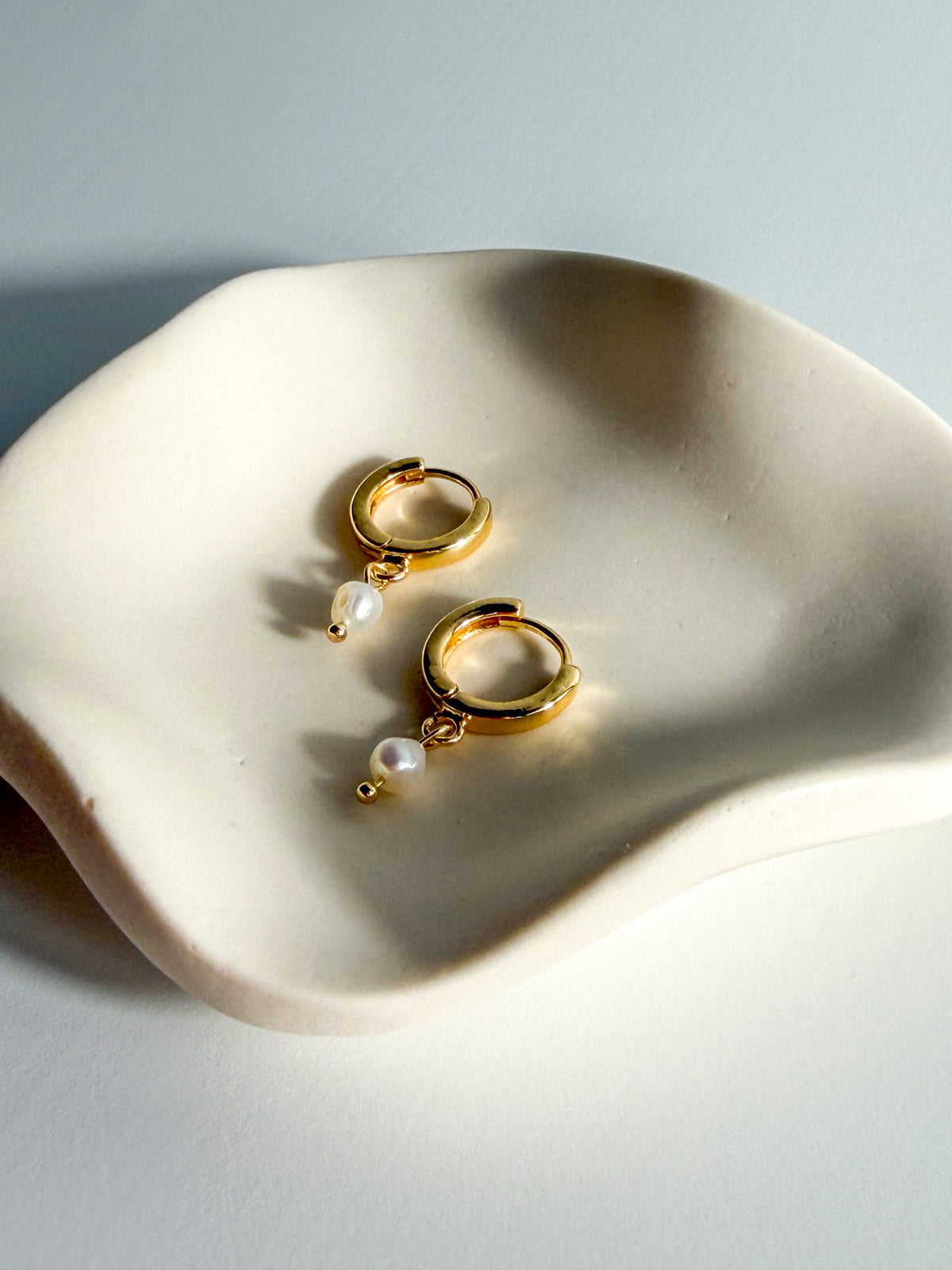 Meli gold-filled hoops with single freshwater pearls, angled detail view on a jewelry tray.