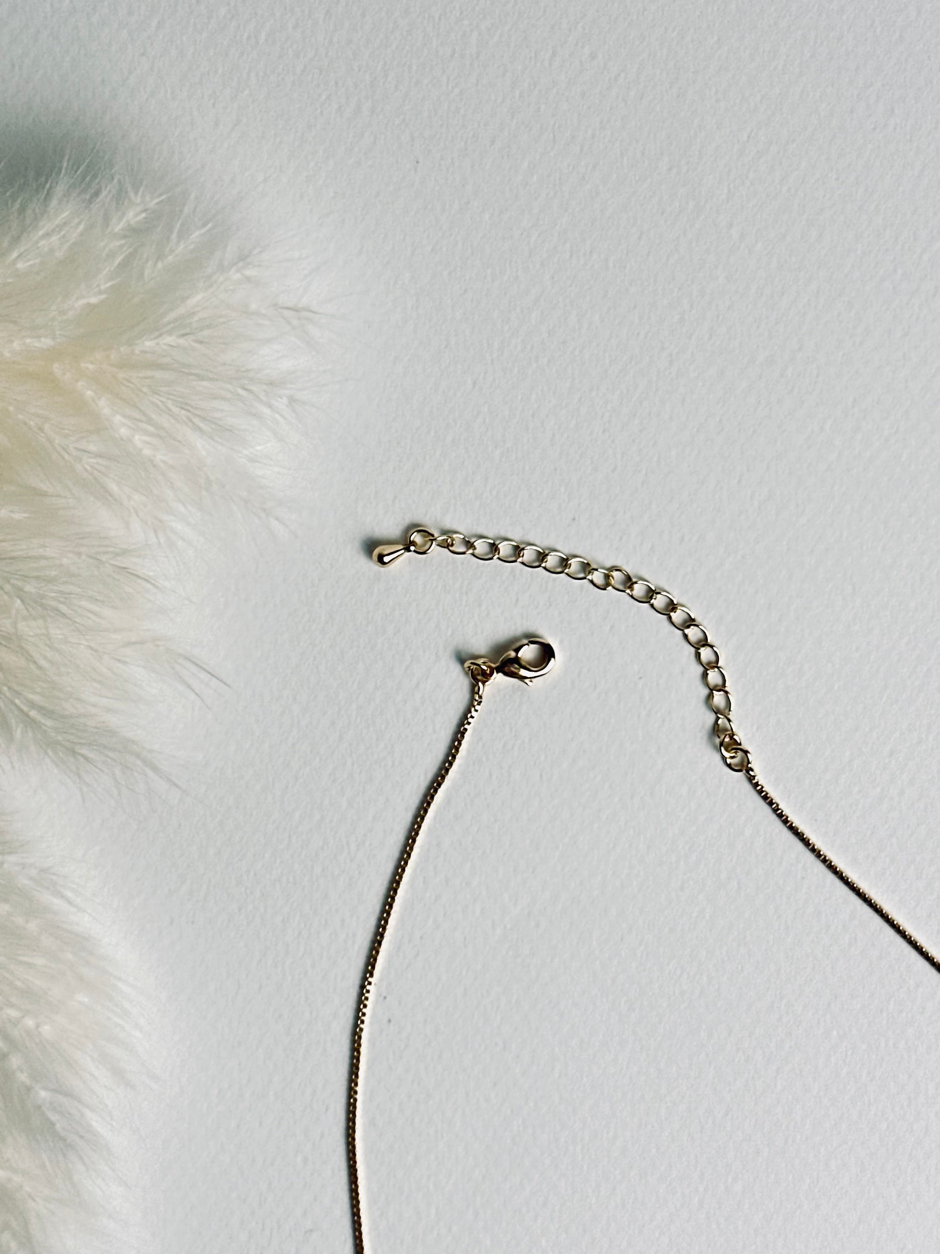 Serena — Gold Box Chain Necklace from the Timeless Grace collection, a thin gold-plated brass chain displayed on a book with focus on the lobster clasp and 2-inch extender. The delicate links and adjustable design highlight both elegance and practicality, symbolizing versatility, grace, and effortless style.