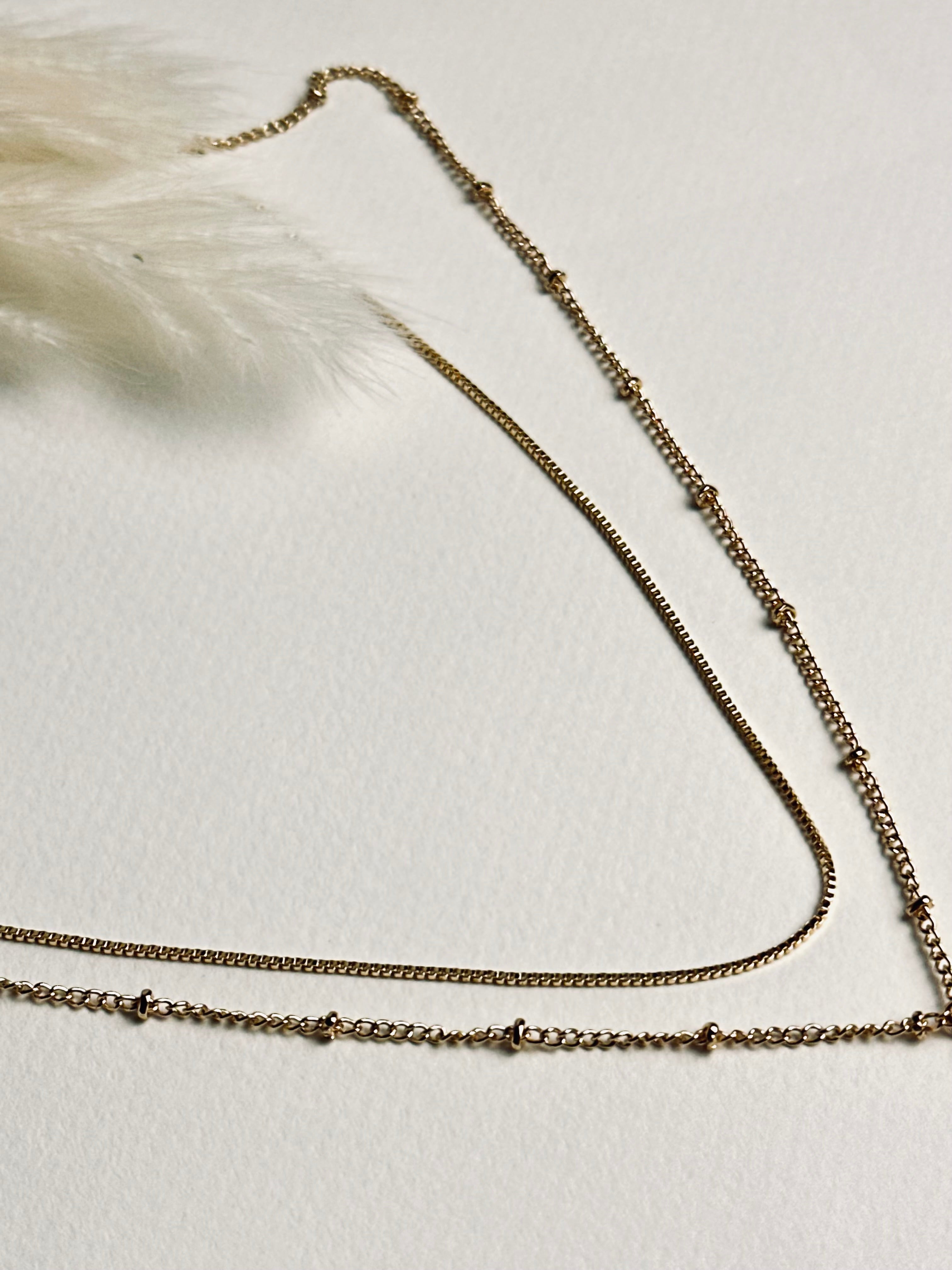 Serena — Gold Box Chain Necklace from the Timeless Grace collection, layered with another delicate gold necklace on a model. The thin gold-plated brass chains create a graceful, sophisticated look, showcasing versatile styling while symbolizing balance, elegance, and subtle self-expression.