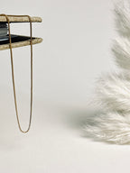 Serena — Gold Box Chain Necklace from the Timeless Grace collection, a thin gold-plated brass chain delicately draped across an open book. The soft light highlights its fine, box-style links, creating a serene and elegant mood — a gentle reminder to pause, breathe, and embrace your quiet strength.